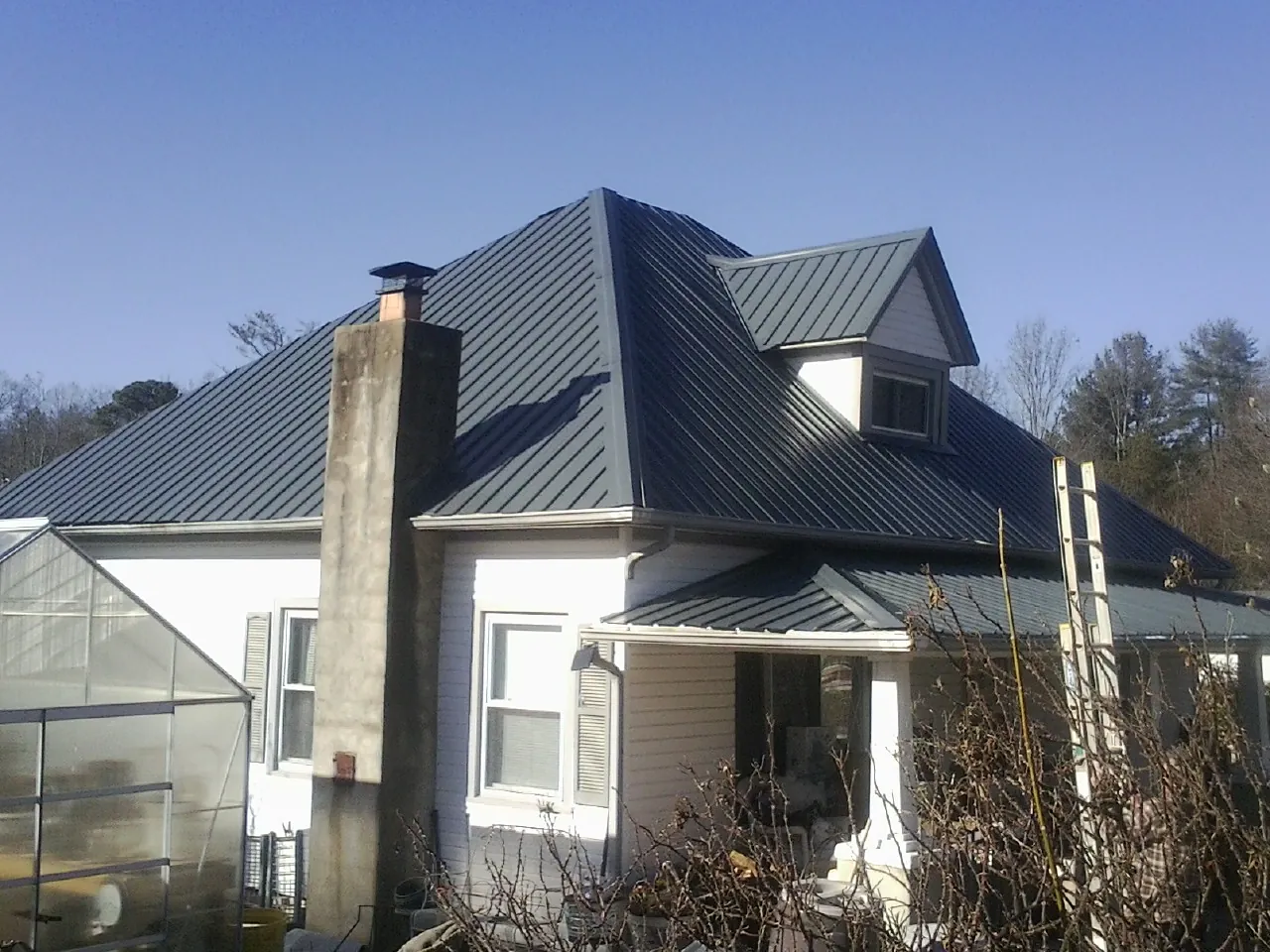 Dark blue standing seam metal roof on a white farmhouse with dormer — Slate & Tile Roof Repair by Roofing Brothers in Rosamond
