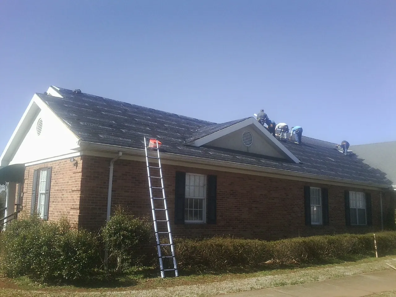 Crew tearing shingles off a brick ranch roof with a ladder set — Metal Roof Repair work by our crew in Rosamond