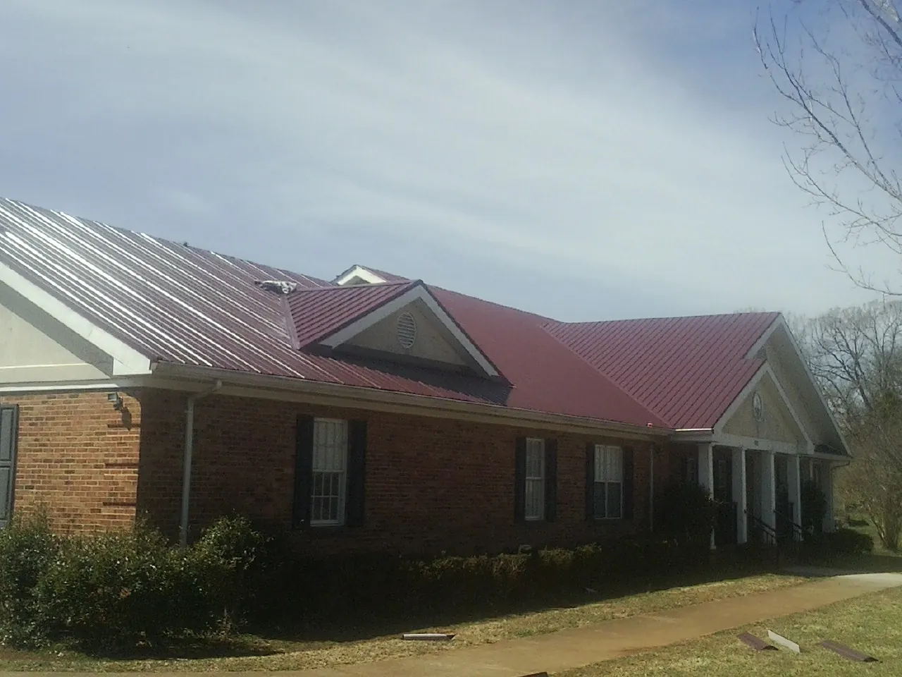 Red metal roof with gabled entries on a long brick building, from a Hail Damage Roof Repair job in Rosamond