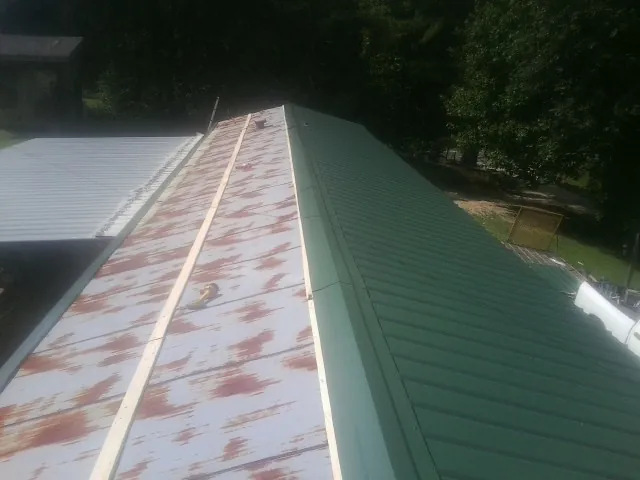 Old rusted panels beside newly installed green metal roofing — Wind Damage Roof Repair by Roofing Brothers in Rosamond