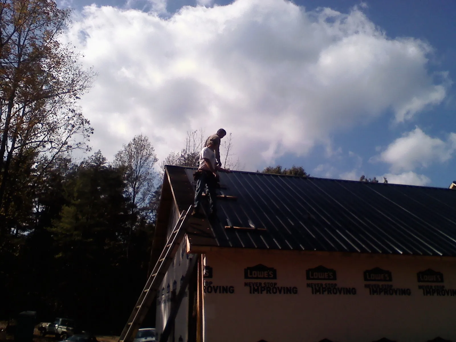 Roofer fastening dark metal panels high against a cloudy sky, from a Roof Inspection job in Rosamond