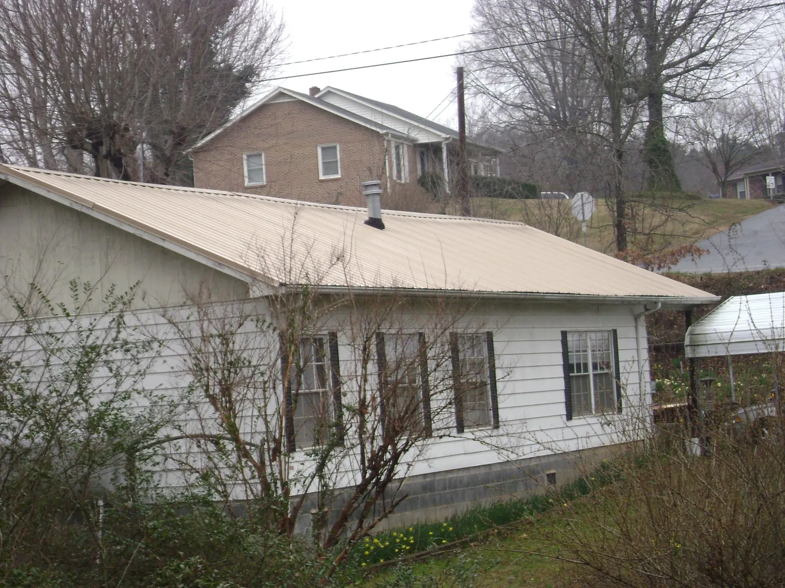 Tan metal roof on a white sided house set into a hillside — Commercial Roofing by Roofing Brothers in Rosamond